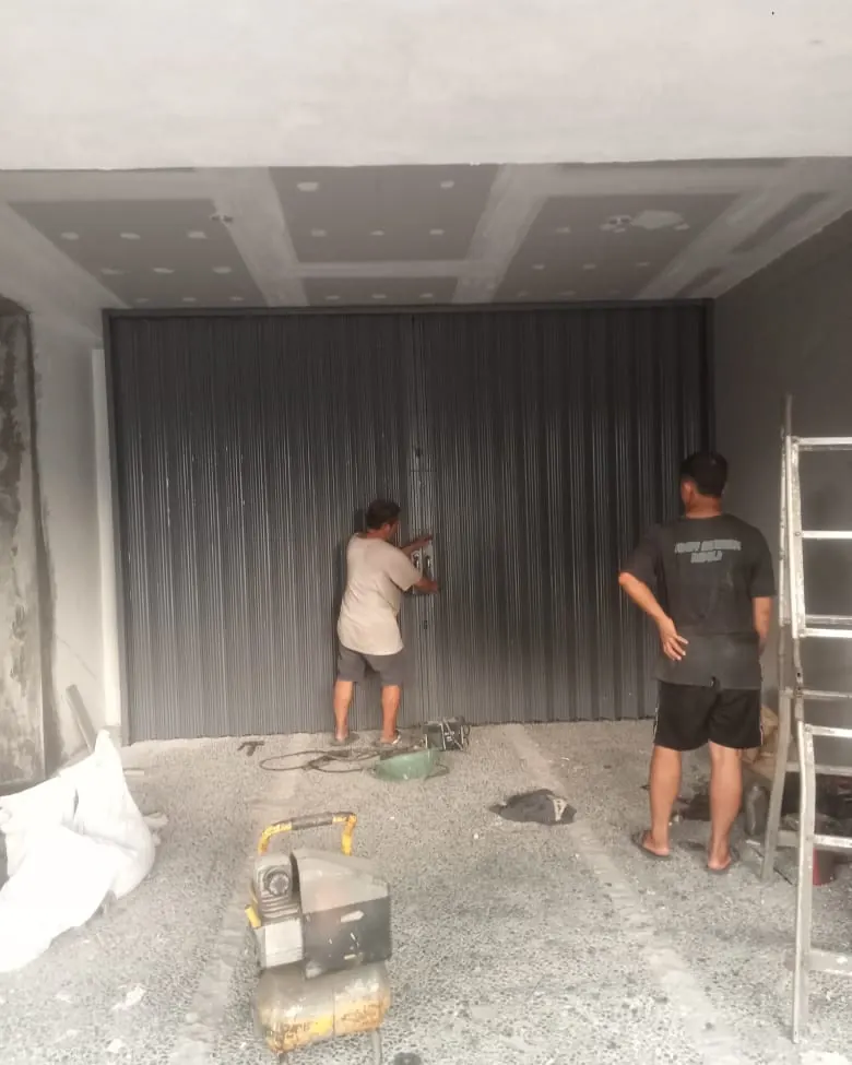 Dua teknisi menyetel folding gate di ruko baru